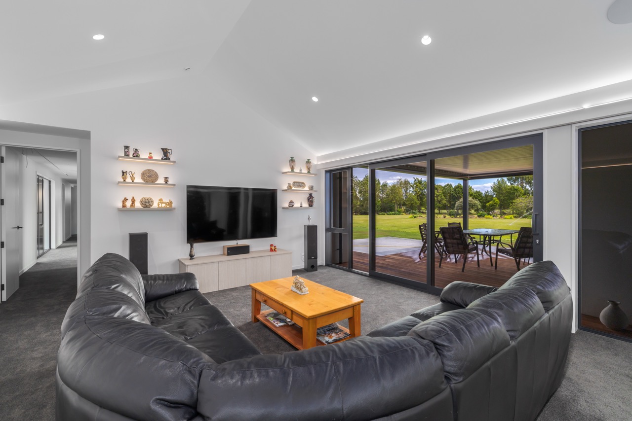 Living room with raked ceiling, LED strip lighting, floating shelves, and floor-to-ceiling sliding doors