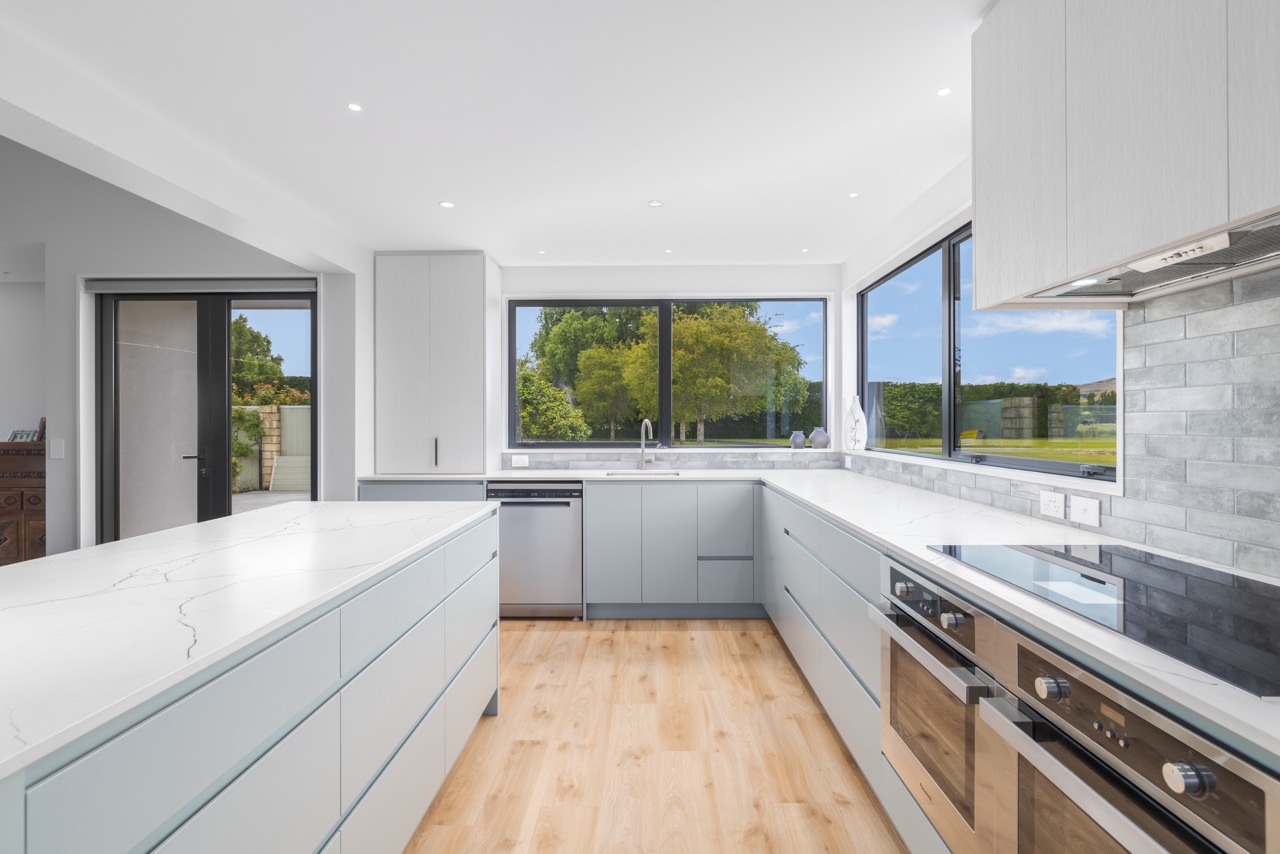 Kitchen detail showing marble benchtop, brick-style splashback, double oven, and rural views through corner windows
