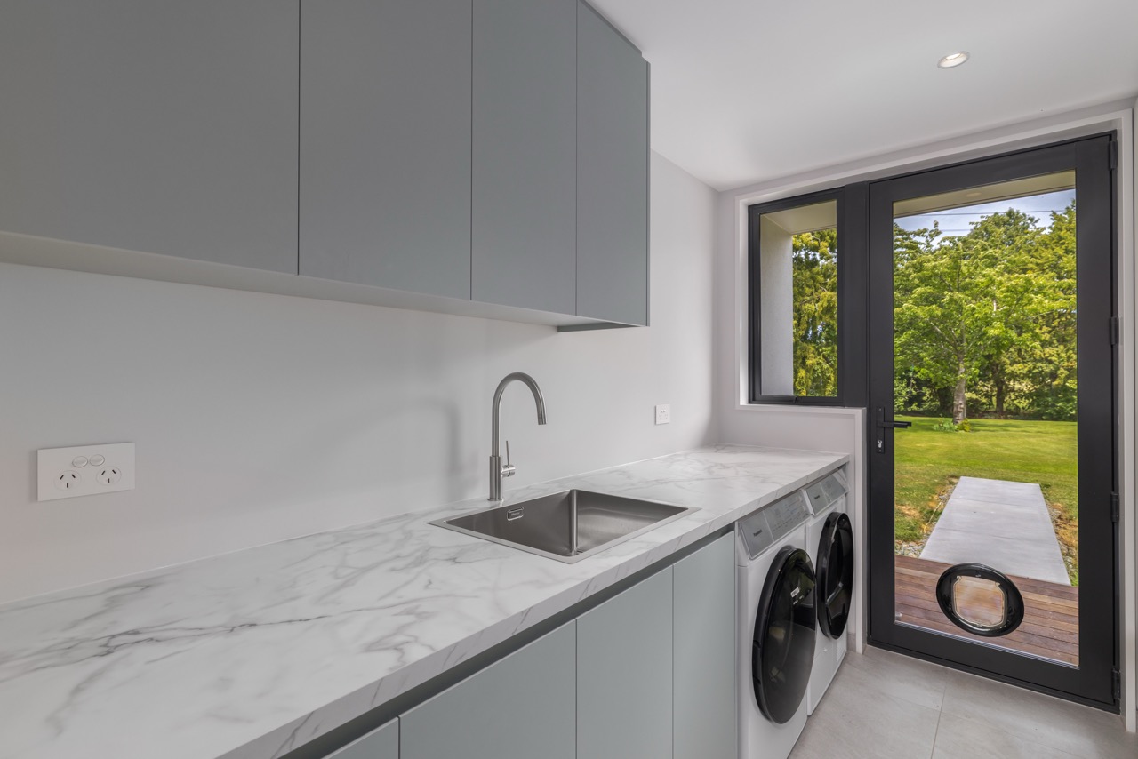 Laundry with sage cabinetry, marble benchtop, and garden-facing glass door