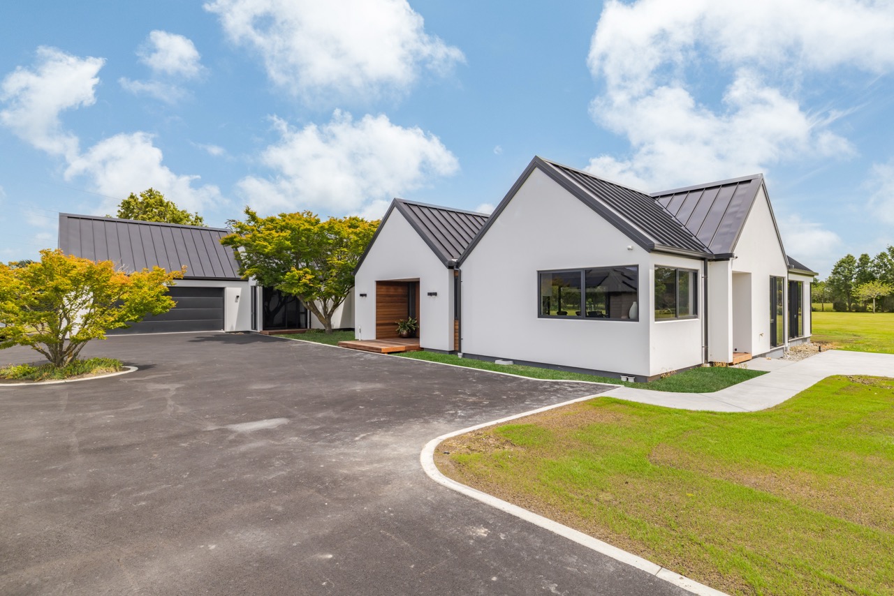 Wide front exterior — multi-gable white plaster home with standing seam roof and circular driveway