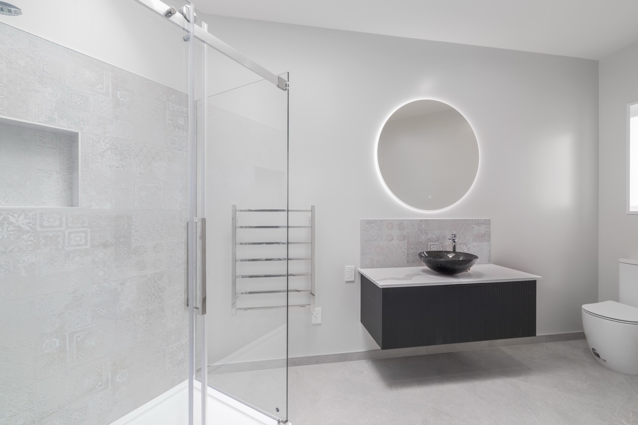 Full bathroom with glass shower, patterned tile, floating vanity, and LED mirror