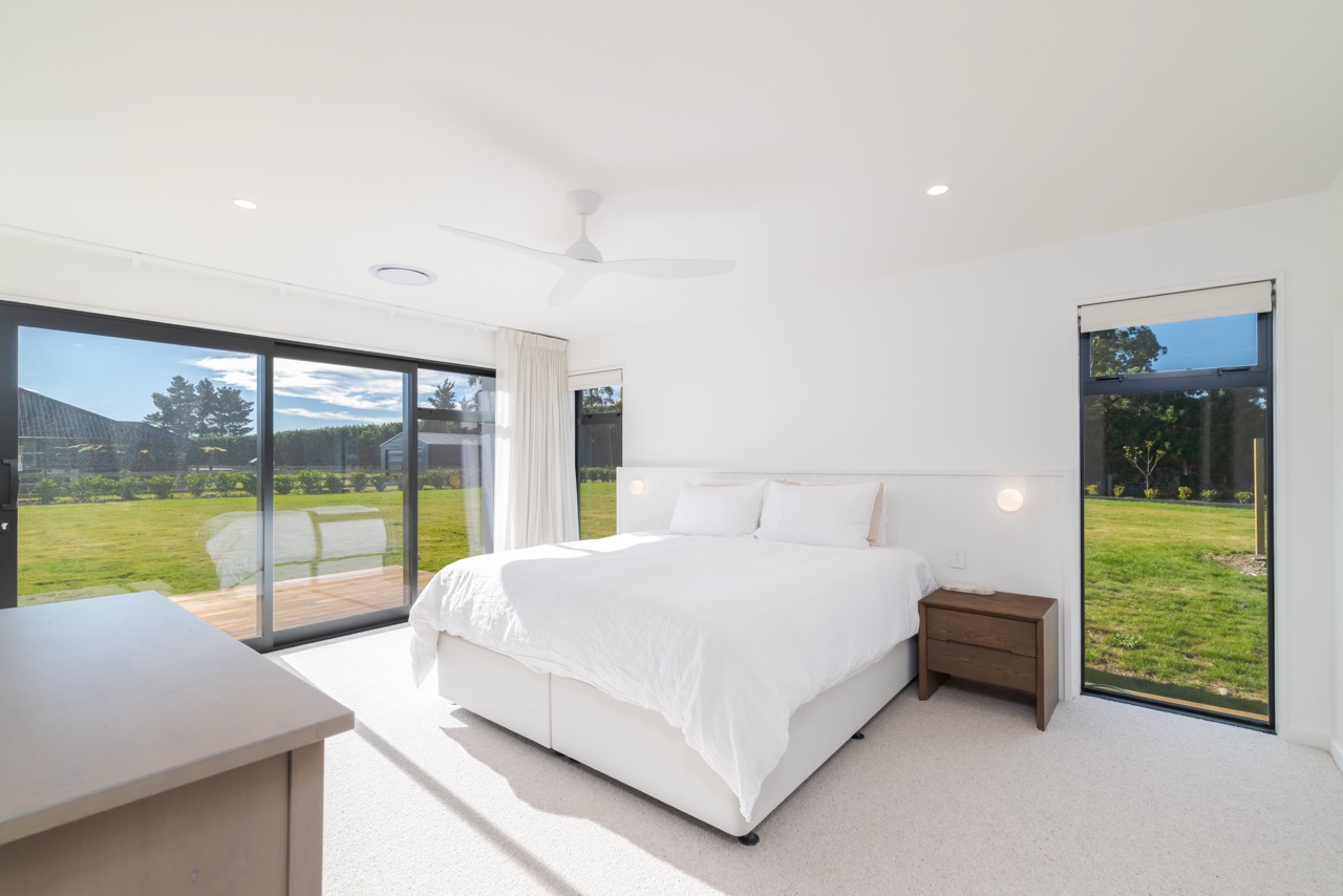 Master bedroom with king bed, ceiling fan, and floor-to-ceiling sliding doors to deck and lawn