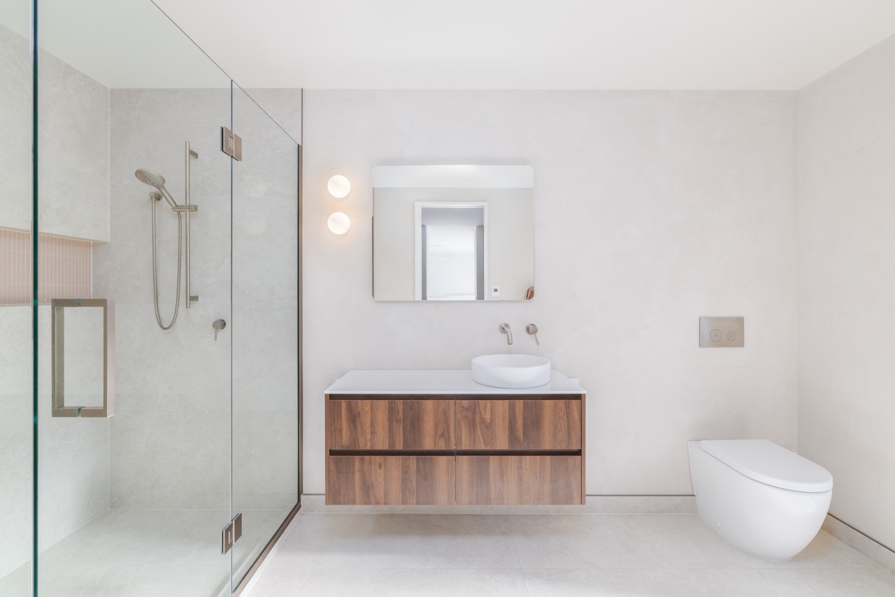 Ensuite vanity with vessel basin, walnut drawers, full-height mirror, and wall-mounted toilet
