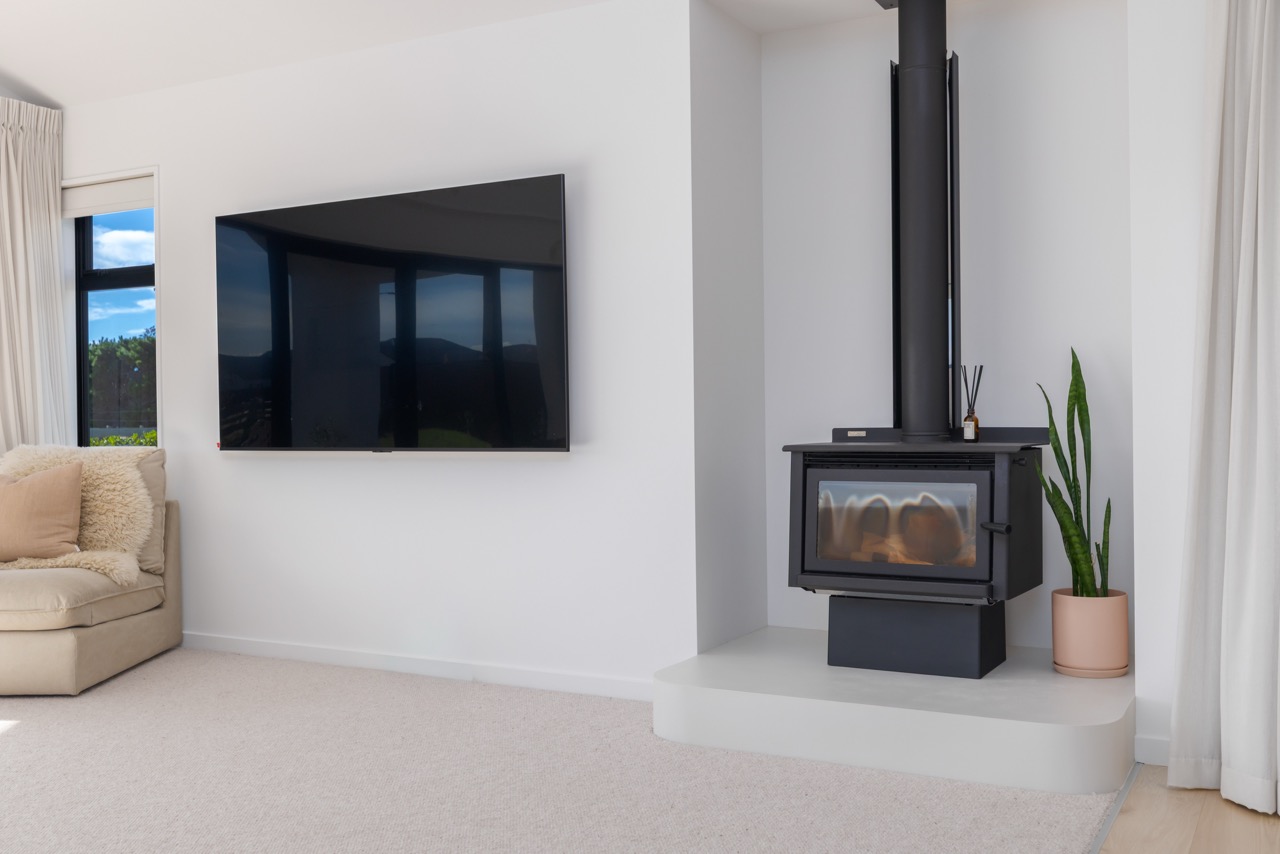 Living room with mounted television, freestanding wood burner, and cream sectional