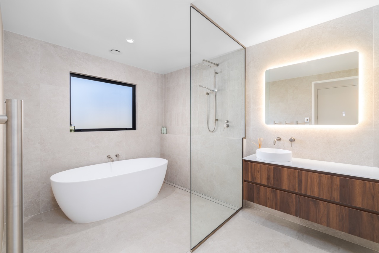 Family bathroom with freestanding bath, walk-in shower with glass partition, walnut floating vanity, and backlit mirror