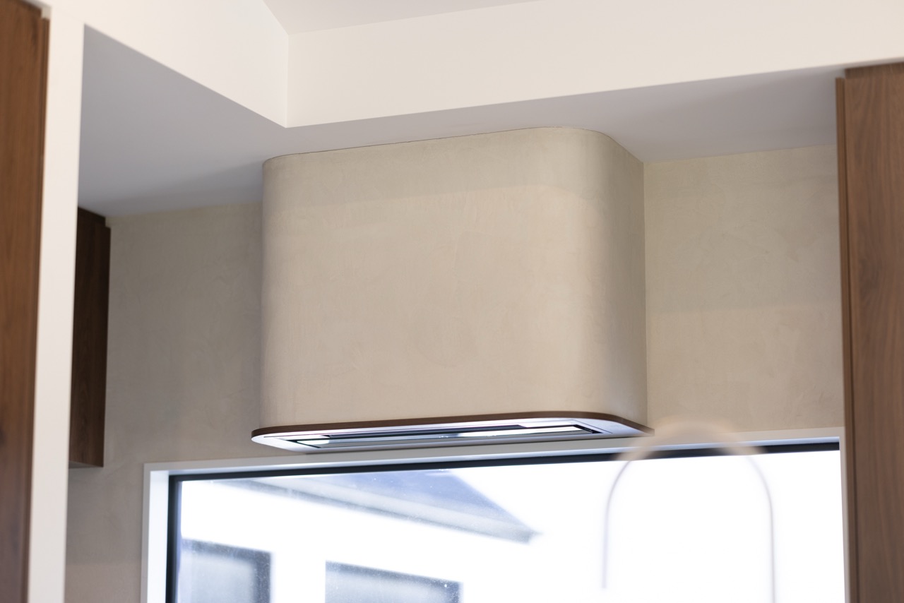 Curved venetian plaster rangehood detail above kitchen window with walnut cabinetry on either side