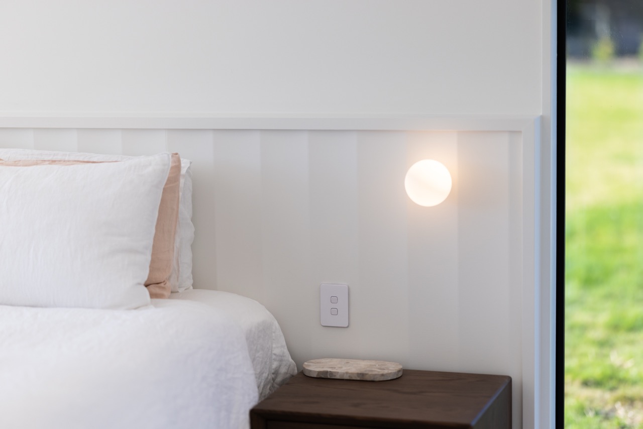Master bedroom side detail — circular wall sconce, board-and-batten panelling, and walnut nightstand
