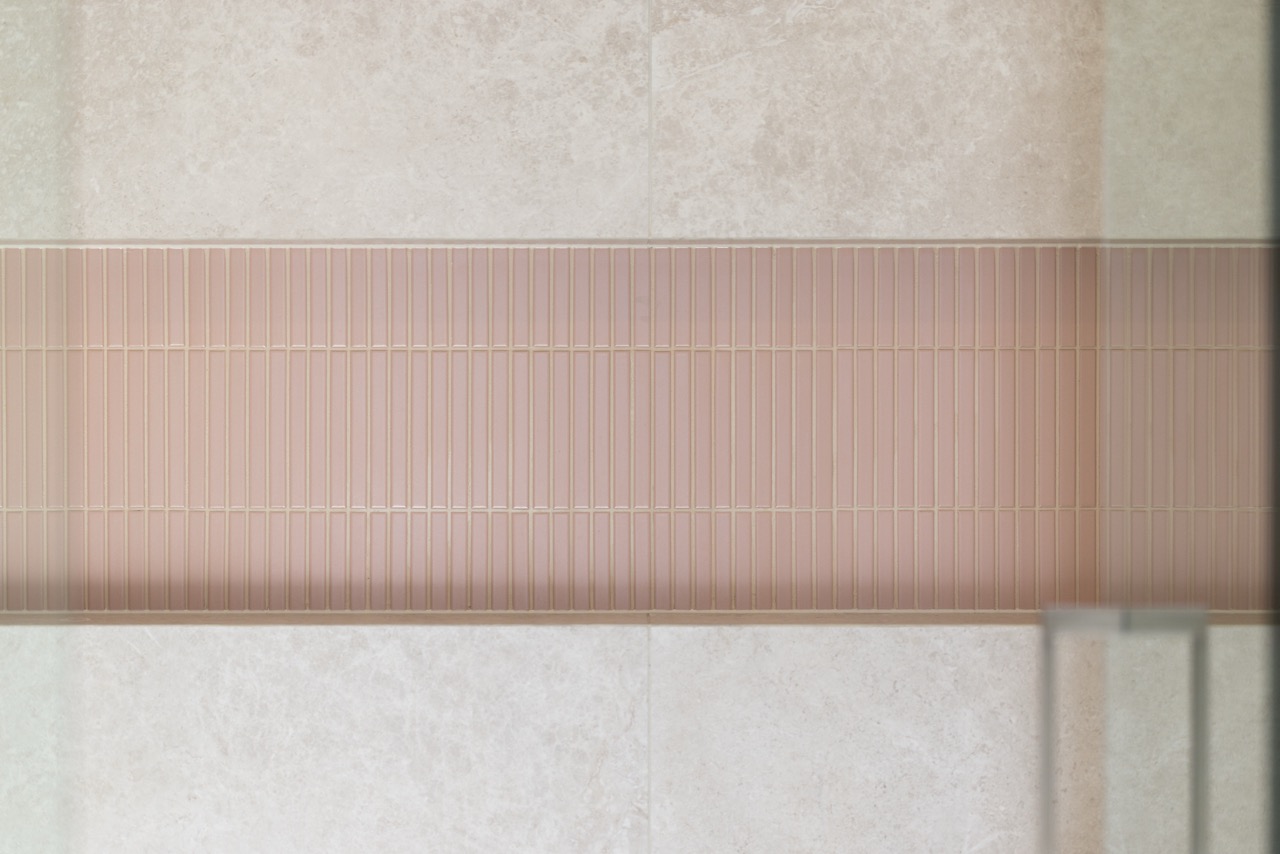 Pink mosaic feature tile band close-up — fingertile pattern across travertine