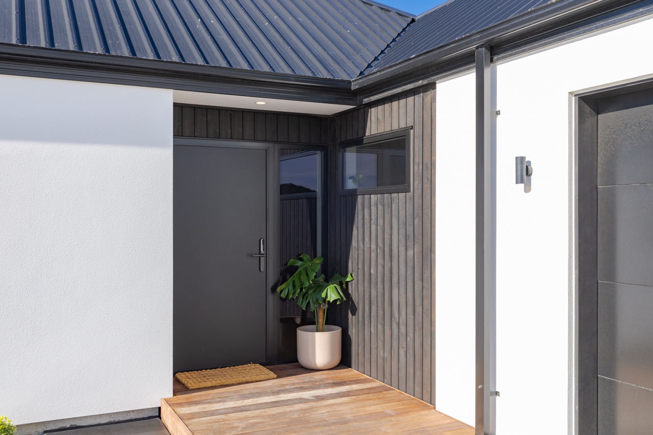 Front entry detail with potted monstera, recessed downlight, and timber soffit