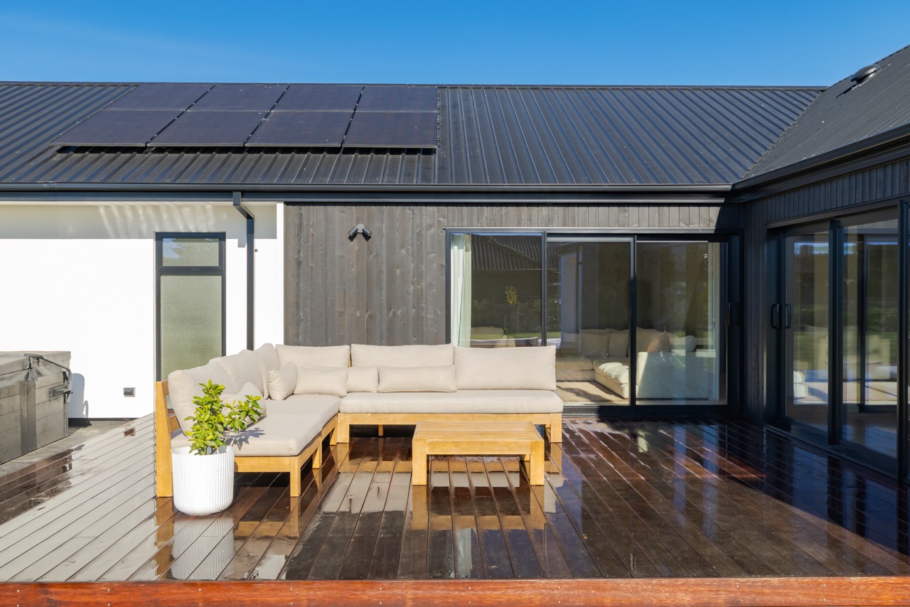 Central courtyard with timber sectional, solar panels above, and dark vertical timber walls